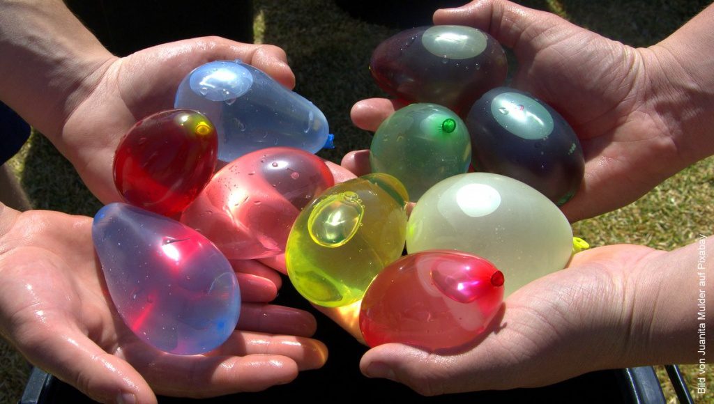 vier Hände halten kleine bunte Ballons mit Wasser gefüllt zum Vergleich