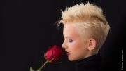 Blonde Frau mit kurzen Haaren riecht an einer roten Rose