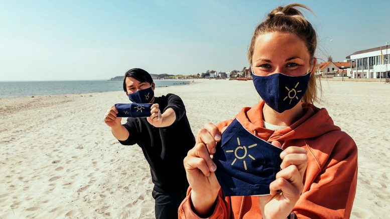 junge Frau und junger Mann am Strand von Grömitz mit den Grömitz-Corona-Masken für die Corona-Lockerungen