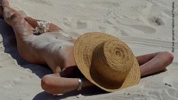 Nackte Frau mit Sonnenhut am Strand