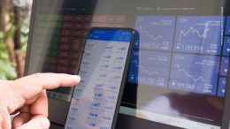 Symbolfoto Trading Monitor und Smartphone mit Kurscharts und einer Hand