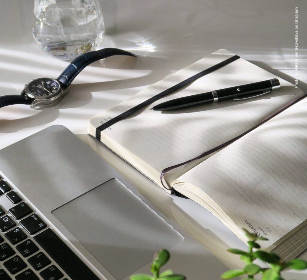 Notizbuch, Uhr, Laptop auf dem Schreibtisch