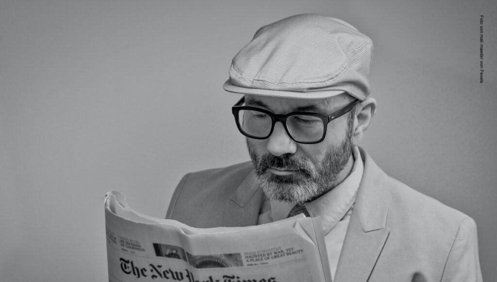 Mann liest Zeitung und hat eine Mütze auf